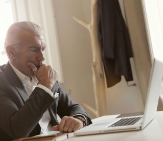 Man in Black Suit  Leaning on White Table